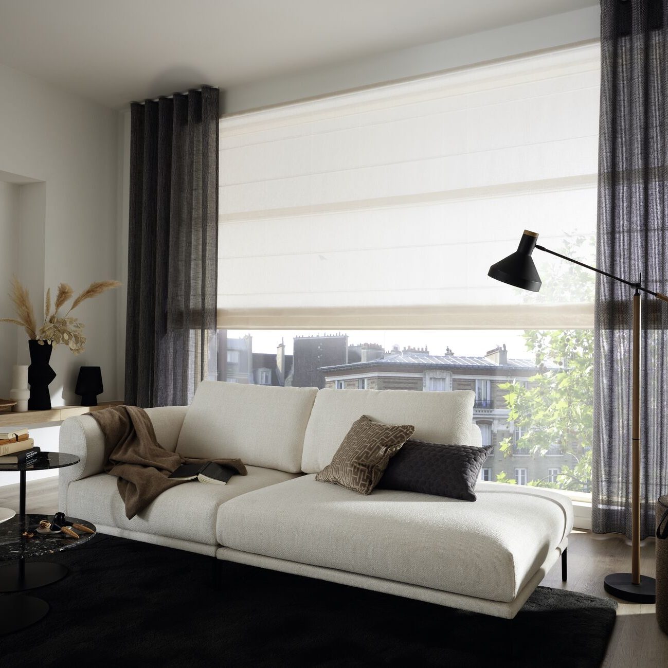 Helles Wohnambiente mit beigem Sofa, Dekokissen und großer Fensterfront mit Faltrollos.