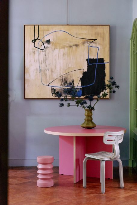 Moderne Inneneinrichtung mit pinkem Tisch, Stuhl und abstrahierter Kunst an der Wand.
