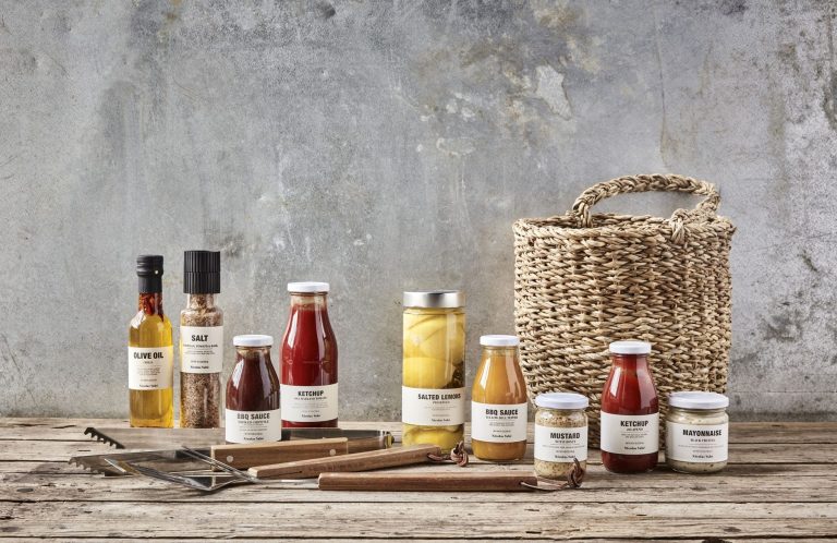 Verschiedene Gläser mit Marmelade, Saucen und ein Korb auf einer Holzoberfläche.