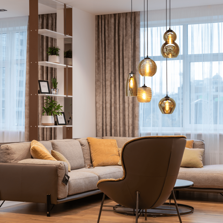 Heller Wohnraum mit grauem Sofa, senffarbenen Kissen und eleganter Hängeleuchte.