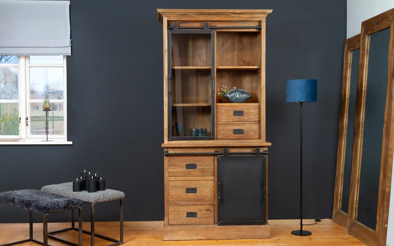 Holländische Teakmöbel Holzschrank mit Glastüren, Schubladen und einer dunkelgrauen Front, vor einer grauen Wand.