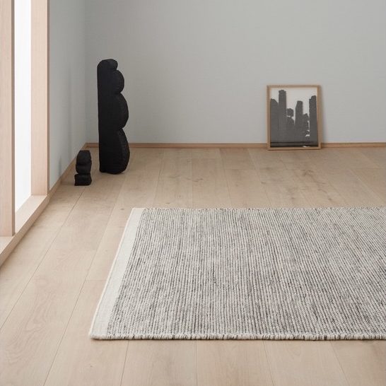 Heller Raum mit Holzfußboden, grauem Teppich, schwarzer Dekoration und einem Rahmen mit Kunst.