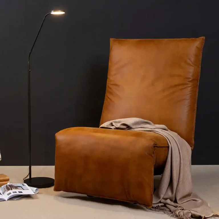 Sessel aus braunem Leder mit Decke und Stehlampe davor vor schwarzem Hintergrund.