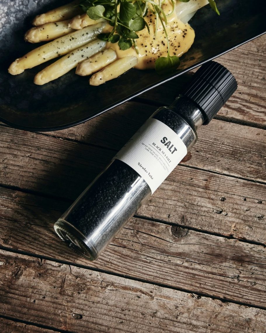 Flasche mit schwarzem Pfeffer neben gekochtem Spargel auf einem rustikalen Tisch.