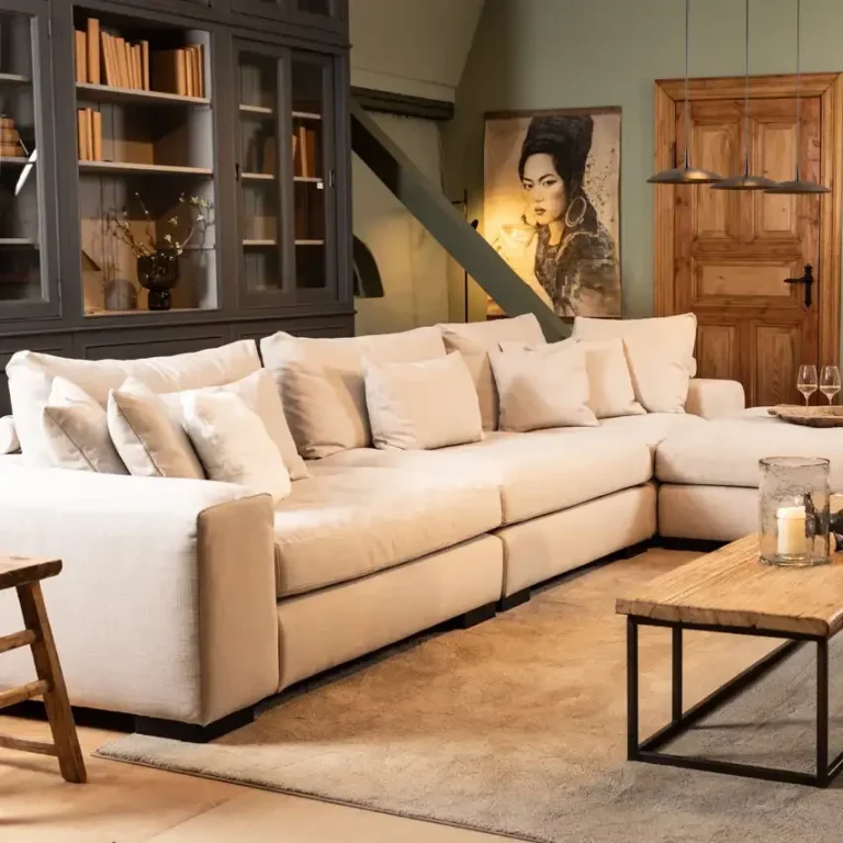 Hellbeige Wohnlandschaft mit Kissen, Holzkaffee Tisch und Wandregal im Hintergrund.