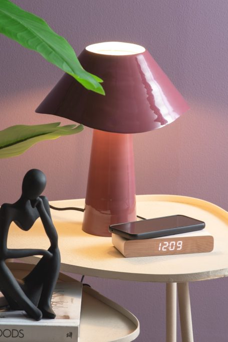 Lila Tischlampe mit runder Schirm, neben einem Smartphone und einer Figur auf einem Beistelltisch.