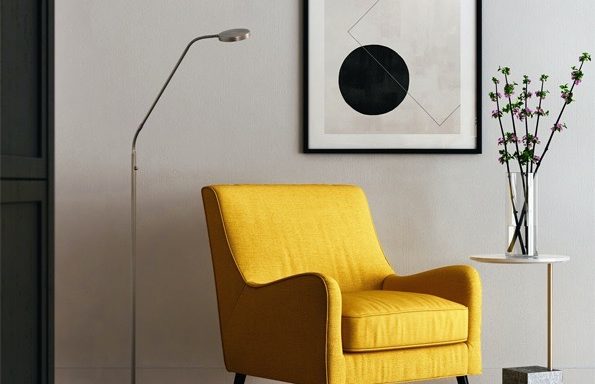 Gelber Sessel neben einer Stehlampe und einem kleinen Tisch mit einer modernen Wandkunst.