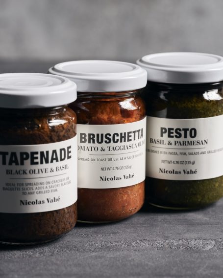 Drei Gläser mit Aufstrichen: Tapenade, Bruschetta und Pesto auf einem grauen Hintergrund.