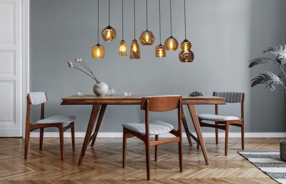 Modern Esszimmer mit Holztisch, Stühlen und hängenden Lampen an einer grauen Wand.