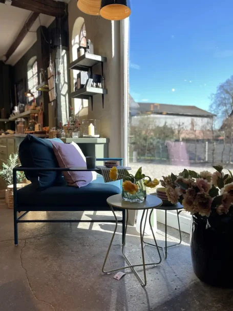 Bequemer Sessel mit Kissen, Tisch und Blumen, Blick auf einen sonnigen Tag draußen.