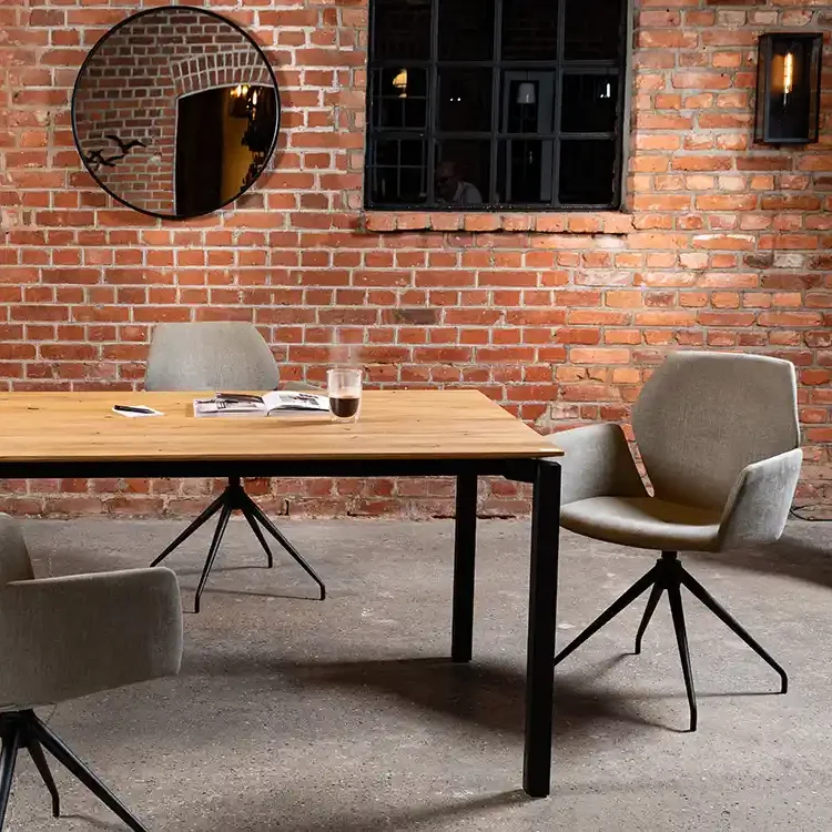 Moderne Essgruppe mit Holztisch, grauen Stühlen und ziegelsteinerner Wand im Hintergrund.